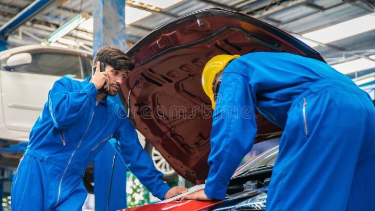 Cuándo acelero suena la banda: Causas y soluciones 1 mecanico revisando el coche del capo abierto con su asistente mientras utiliza un telefono movil para informar problemas de al 242089609